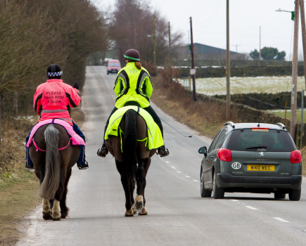 Pictured are two horse riders wearing high vis for safety while hacking along a main road
