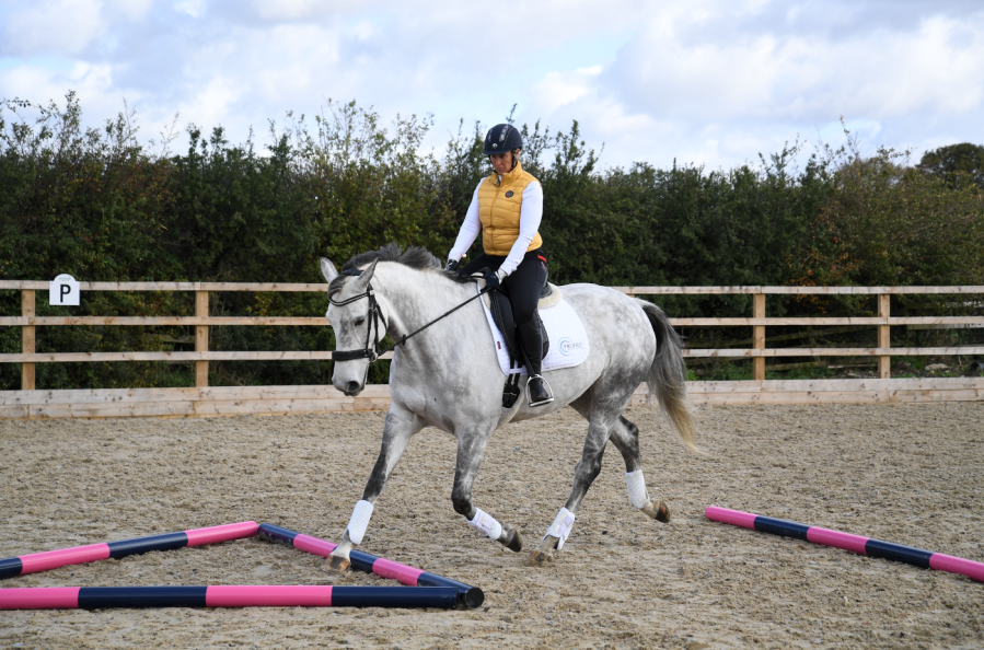 Pictured is a grey horse and rider trotting through a triangle: just one of the fun ground pole exercises for horses that get great results