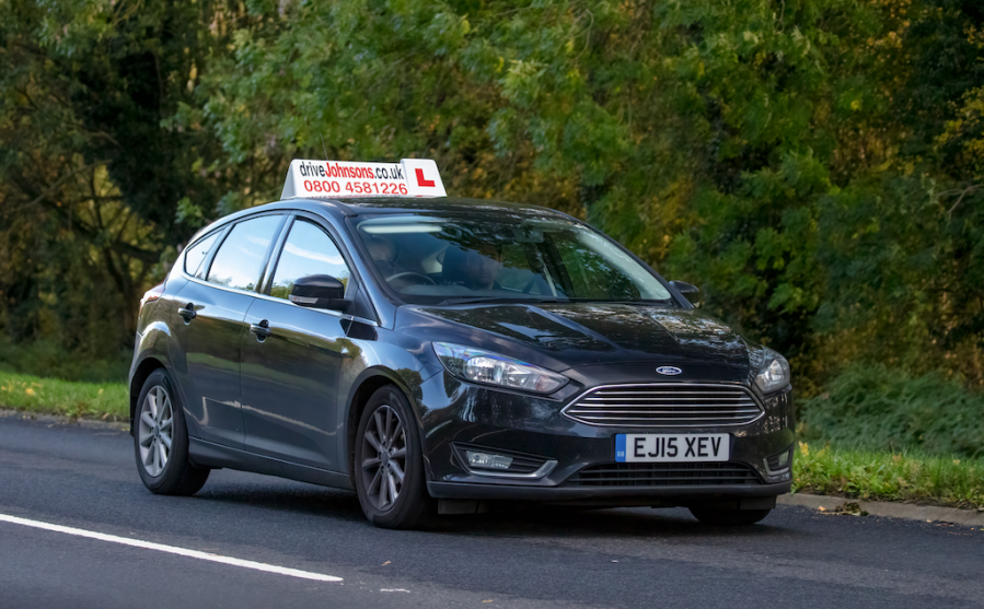 Pictured is a dark car being driven by a learner driver on a main road with a large L on the roof; learner drivers need to be educated about how to pass horses safely on the road