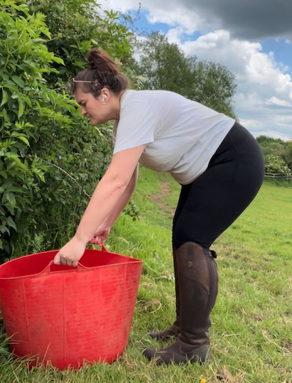 Pictured is tester Natalie wearing the Mountain Horse Wild River Tall Boots while filling a red water bucket in a horse's field